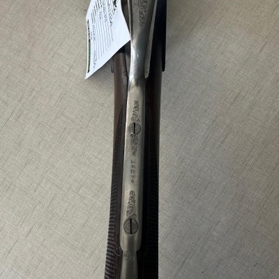 Espingarda metálica prateada e madeira com etiqueta pendurada