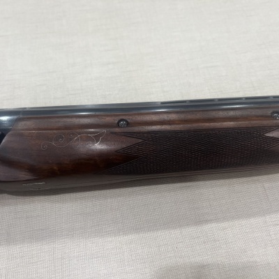 Detalhe de arma de caça em madeira e metal sobre tecido claro