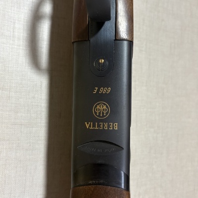 Espingarda Beretta 686 E com cabo de madeira castanha e corpo preto com gravações douradas