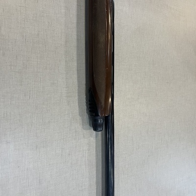 Espingarda com coronha de madeira castanha e cano preto junto a parede clara
