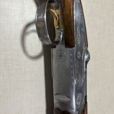 Parte lateral de arma com madeira castanha e detalhes metálicos gravados