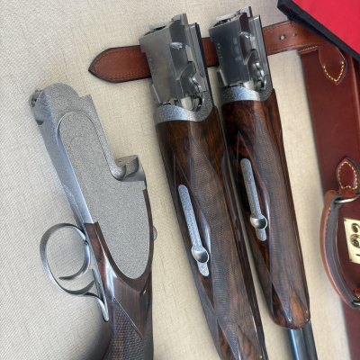 Três espingardas de caça com coronhas em madeira e punhos metálicos sobre uma superfície clara