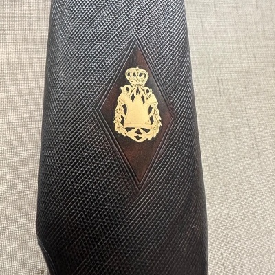 Coronha de arma em madeira escura com textura e brasão dourado