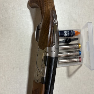 Espingarda Beretta com acessórios incluindo óleo e chokes em caixa transparente.