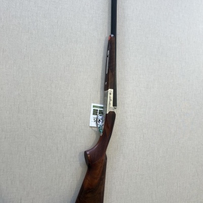 Espingarda com coronha de madeira castanha escura e cano longo negro encostada numa parede clara