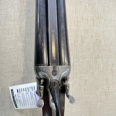 Espingarda antiga de canos duplos sobre fundo bege.