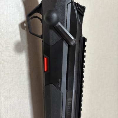 Rifle preto BERETTA BRX-4 com detalhe vermelho encostado numa parede clara