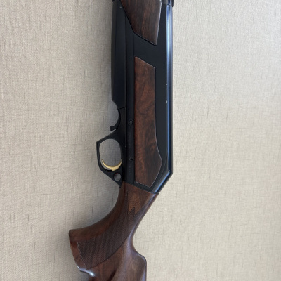 Parte de um rifle com coronha em madeira castanha escura e corpo em metal preto com disparador dourado