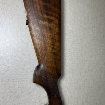 Coronha de madeira polida de arma de fogo com detalhe texturizado e gatilho dourado sobre superfície clara