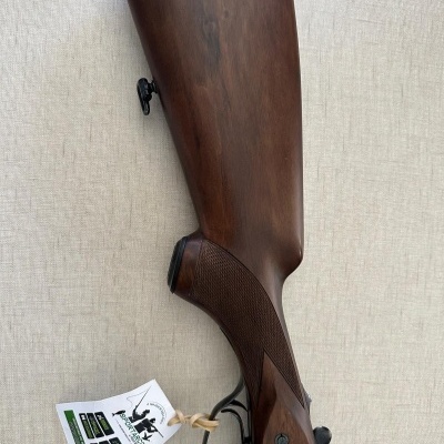 Espingarda de madeira castanha com etiqueta branca pendurada sobre fundo claro.