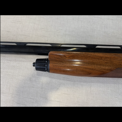 Espingarda com coronha de madeira e cano preto sobre tecido cinzento.