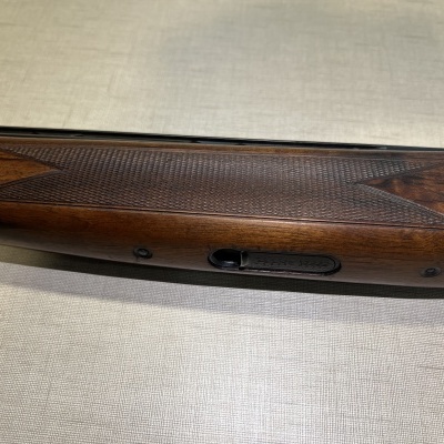 Empunhadura de arma de fogo em madeira castanha com padrão texturizado.