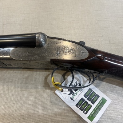 Espingarda de canos paralelos com coronha de madeira e acabamento metálico gravado com etiqueta pendurada