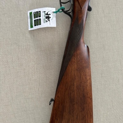 Coronha de espingarda em madeira com parte metálica prateada e etiqueta pendurada