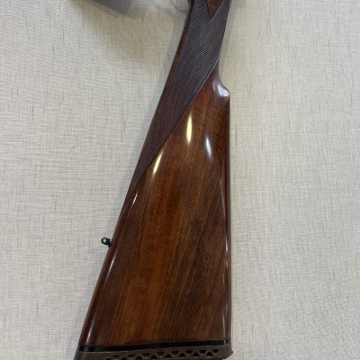 Espingarda com coronha em madeira escura e etiqueta pendurada sobre superfície clara