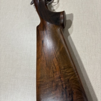 Coronha de arma de fogo em madeira castanha escura com detalhes metálicos prateados.