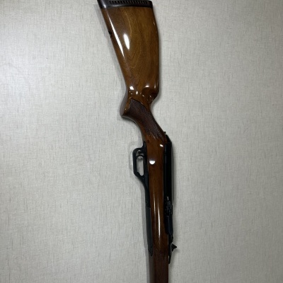 Carabina de madeira polida com detalhes em metal preto encostada numa parede clara