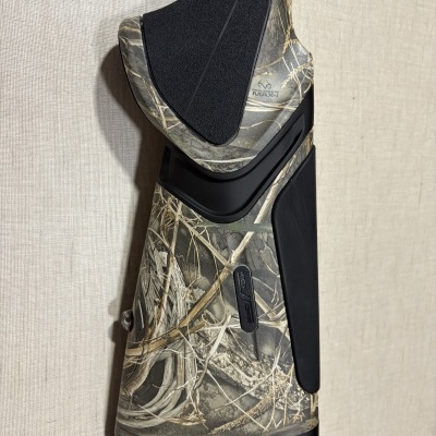 Arma com padrão camuflado e textura em borracha e plástico sobre fundo claro.