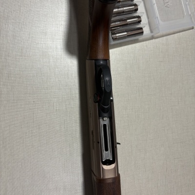 Espingarda com cabo de madeira, corpo metálico e caixa plástica com acessórios.