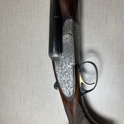Espingarda de canos duplos com detalhes gravados e coronha em madeira escura sobre superfície clara