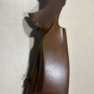 Coronha de arma de madeira polida com textura quadriculada e suporte metálico para alça