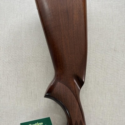 Coronha de espingarda de madeira castanha com proteção preta de borracha e cartão verde de identificação.