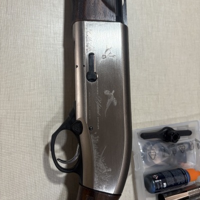 Espingarda metálica cinza com cabo de madeira e acessórios em caixa plástica transparente