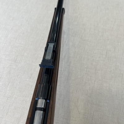 Espingarda metálica preta com coronha de madeira escura sobre superfície clara