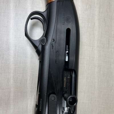 Espingarda Beretta com corpo preto fosco e coronha em madeira sobre tecido claro