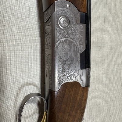 Arma de fogo com cabo em madeira e corpo metálico gravado com motivos florais e pássaro.