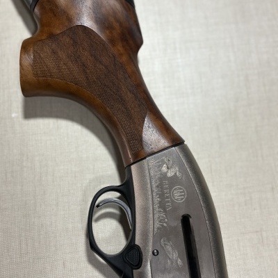 Parte traseira e gatilho de espingarda Beretta com coronha em madeira castanha e corpo metálico cinzento gravado