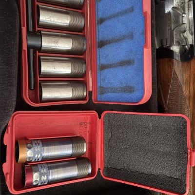 Estojo com peças metálicas cilíndricas e cápsulas perto de arma