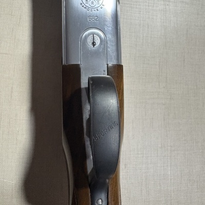 Parte superior de arma de fogo de metal prateado e madeira castanha com inscrições.