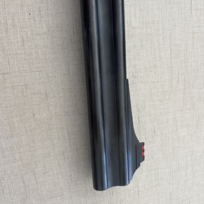 Arma de fogo de cano duplo preto com detalhe vermelho sobre superfície cinzenta