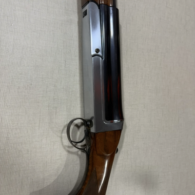 Espingarda de caça em madeira castanha e metal prateado colocada contra parede clara