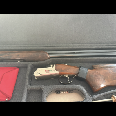 Espingarda de cano duplo com coronha de madeira e inscrição 'Barazi High Tech' numa mala preto acolchoada