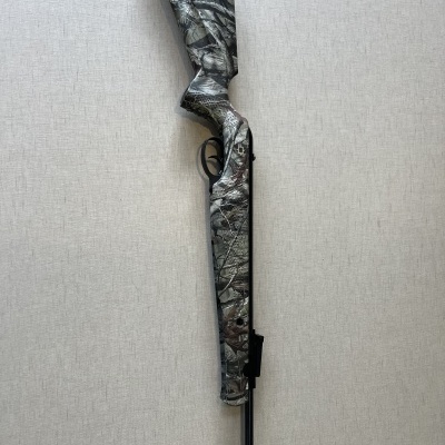 Espingarda camuflada encostada numa parede clara