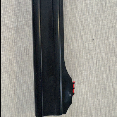 Peça metálica preta com três detalhes vermelhos numa extremidade sobre tecido cinzento.