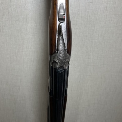 Espingarda em madeira e metal com detalhes gravados inclinada contra parede clara