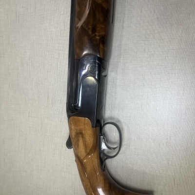 Espingarda de caça com madeira polida e armação metálica preta sobre superfície clara