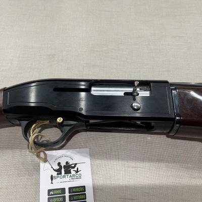 Espingarda com madeira escura e corpo metálico preto sobre tecido bege com etiqueta Sportarco