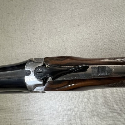 Espingarda de canos duplos com madeira escura e armação metálica prateada.
