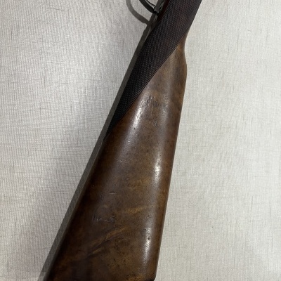 Espingarda com coronha em madeira castanha e detalhes pretos sobre tecido claro