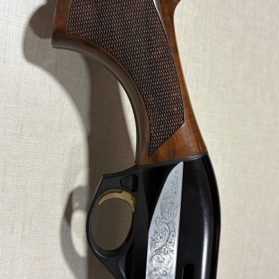 Coronha de espingarda com madeira castanha e decoração gravada em metal preto e prateado.