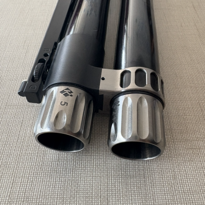 Canos de arma de fogo preto e prata com detalhes gravados sobre superfície bege.