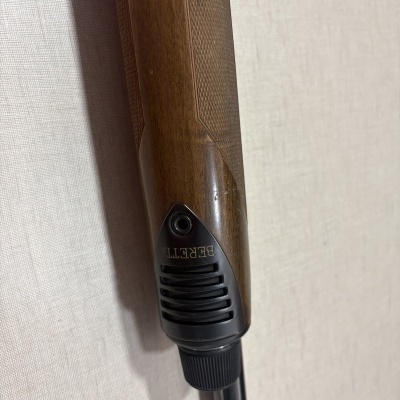 Parte de arma com coronha em madeira castanha e peça preta com escrita BERETTA