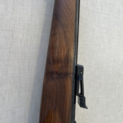 Coronha de madeira de arma de fogo com textura quadriculada e peça metálica ajustável em parede clara