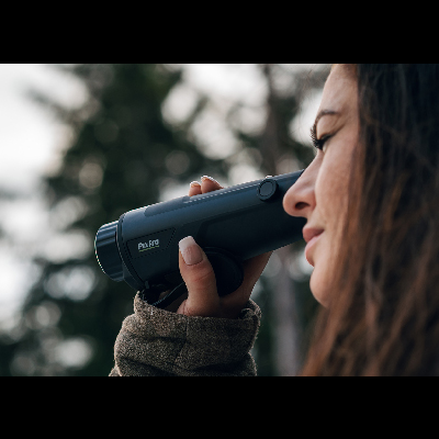 Pessoa segurando monocular preto PuLuz ao ar livre com árvores ao fundo