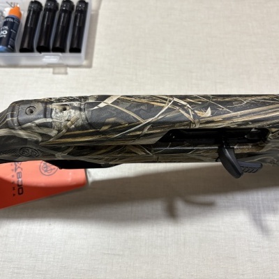 Arma de caça camuflada com acessórios numa mesa clara