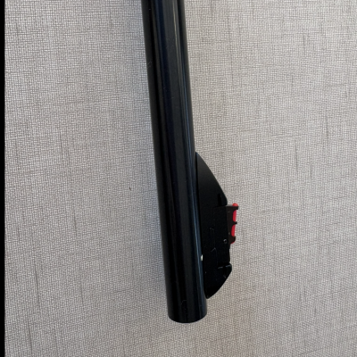 Objeto cilíndrico preto com detalhe vermelho e componente preto contra fundo cinza